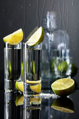 Glasses of tequila with lime and salt on the black reflective background.