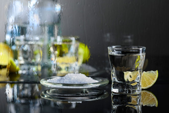 Glass of tequila with lime and salt on the black reflective background.