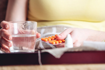 Thermometer pills water and lemon on tray. Person with a cold is treated in bed. Colds, flu and timely treatment