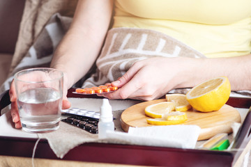 Obraz na płótnie Canvas Thermometer pills water and lemon on tray. Person with a cold is treated in bed. Colds, flu and treatment