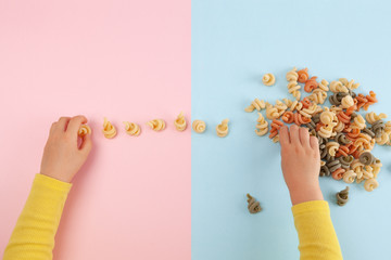 Girl's hands playing with Funghetto veggie pasta on colored table with copy space