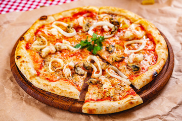 Italian Pizza with seafood and mozzarella cheese on wooden cutting board. Close up