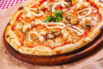 Italian Pizza with seafood and mozzarella cheese on wooden cutting board. Close up