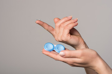 Soft contact lens and blue container in female hands on gray background - obrazy, fototapety, plakaty