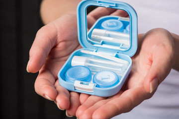 Beautiful hands hold soft contact lenses and a container for them.