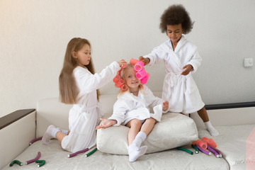 Little girls play with hair curlers and hairpins. Girls girlfriends in white coats braid curlers...