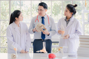 A handsome professor doctor teaching couple of beautiful young asian girl collage student in white laboratory gown learning anatomy class.  Anatomic bone of  hand in biology classroom in university.