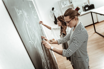 Handsome long-haired dressmaker in eyeglasses and a pretty model looking busy