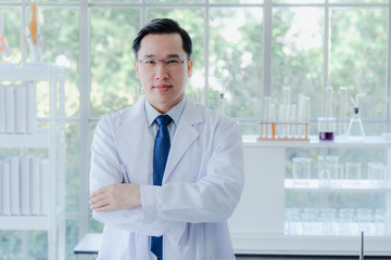 A middle aged man scientist smiling happily with his arms crossed posing at her laboratory colleagues. A confident professor CEO standing preparing equipment for teaching collage student. Copy space.