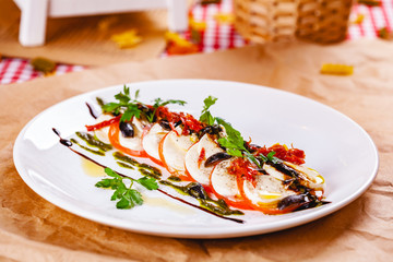 Caprese salad with tomatoes, mozzarella cheese, pesto sauce and black olives on white plate. Close up