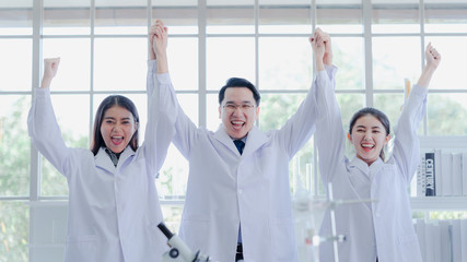 The powerful scientists hold hands raised in colleague lab. They are smiling congratulation for success experiment in biotechnology and pharmacy in career. Science, chemist, biology education concept.