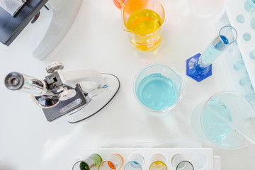 Closed up microscope with tube glass and beaker in laboratory. Blue chemist in glass tubes on white table. Top view of lab in experiment for biotechnology and pharmacy for human life concept.
