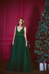 Winter holidays, celebration and people concept - young sexy woman in elegant green evening dress over christmas interior background