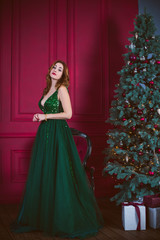 Winter holidays, celebration and people concept - young sexy woman in elegant green evening dress over christmas interior background