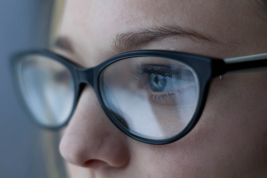 Close-up shot of woman eyes in glasses reflecting a working computer