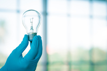 Hand with lab blue glove hold light bulb. Selective focus on detail inside lamp. Laboratory and science concept.