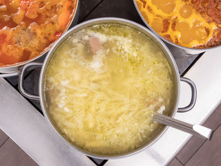 Shurpa soup in a large pan on the stove, next to other soups, top view