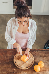 high angle view of woman cutting orange by knife on wooden board in kitchen