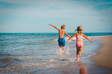 little girl and boy run fly play with waves on beach