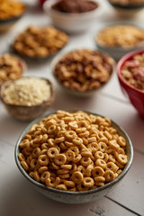 Close up and selective focus. Composition of different kinds cereals placed in ceramic bowls with cornflakes, granola, cereals and oatmeal. Flat lay, top view on white wooden table.