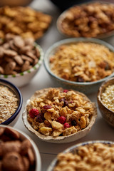 Close up and selective focus. Composition of different kinds cereals placed in ceramic bowls with cornflakes, granola, cereals and oatmeal. Flat lay, top view on white wooden table.