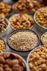 Close up and selective focus. Composition of different kinds cereals placed in ceramic bowls with cornflakes, granola, cereals and oatmeal. Flat lay, top view on white wooden table.