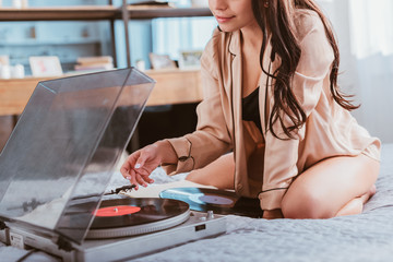 partial view of young woman turning on vinyl audio player while sitting on bed at home