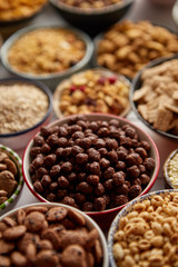 Close up and selective focus. Composition of different kinds cereals placed in ceramic bowls with cornflakes, granola, cereals and oatmeal. Flat lay, top view on white wooden table.