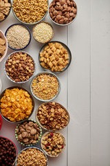 Obraz na płótnie Canvas Assortment of different kinds cereals placed in ceramic bowls with cornflakes, granola, cereals and oatmeal. The concept of breakfast food. Flat lay, with copy space, top view on white wooden table.