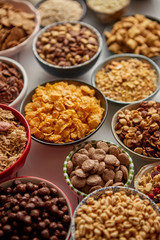 Assortment of different kinds cereals placed in ceramic bowls with cornflakes, granola, cereals and oatmeal. The concept of breakfast food. Flat lay, top view on white wooden table.