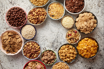 Assortment of various kinds cereals placed in ceramic bowls with cornflakes, granola, cereals and oatmeal. Flat lay, top view on white rusty table with copy space in the middle