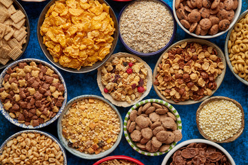 Assortment of various kinds cereals placed in ceramic bowls with cornflakes, granola, cereals and oatmeal. Flat lay, top view on blue rusty table with copy space in the middle