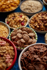 Assortment of various kinds cereals placed in ceramic bowls with cornflakes, granola, cereals and oatmeal. Flat lay, top view on blue rusty table with copy space in the middle