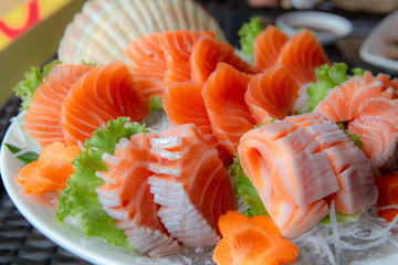 A full size for traditional Japanese food name “Sashimi” included orange with white strip belly and meet served on white big bowl on ice, decorated with carrot flower shaped. Top view shot.