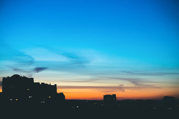 Cityscape with wonderful varicolored vivid dawn. Amazing dramatic blue sky with purple and violet clouds above dark silhouettes of city buildings. Atmospheric background of orange sunrise. Copy space.