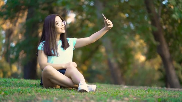 The girl is taking pictures of herself on the phone. Beautiful teen girl doing selfie. The girl makes selfie.