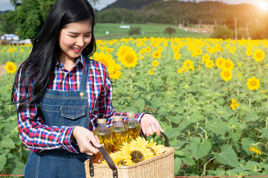 Girl in blue plaid shirt holding a basket with three bottles of sunflower oil - Image