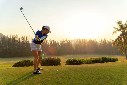 Asian woman golf player doing golf swing tee off on the green sunset evening time, she presumably does exercise. 