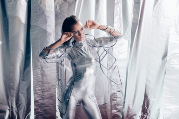 elegant young woman posing in silver bodysuit and raincoat on metallic background