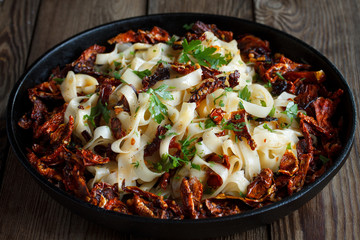 Sun-dried tomatoes with pasta, parsley in an iron black pan on a natural wooden background. Close up