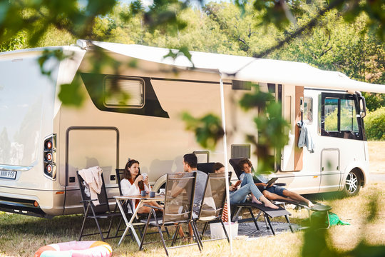 Family relaxing on chairs outside camper van at campsite during summer vacation
