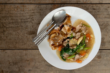 Fried noodle with pork and broccoli or Rad Na Moo in Thailand on White plate placed on wooden floor.