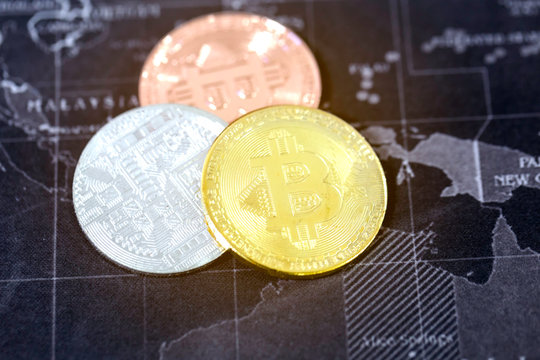 Triple of gold, silver, bronze Bitcoin coins on world map. Selective focus on golden. Virtual cryptocurrency concept..