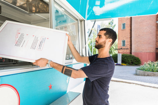 Side view of confident young male salesman holding menu placard at food truck