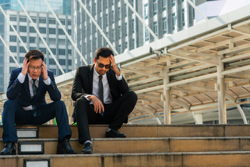 Asian business man sitting on a staircase between a tall building, stressed and fear by a business...