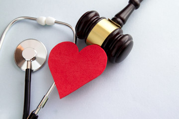 Gavel with red heart, pills, stethoscope and books on table. Medical law concept.
