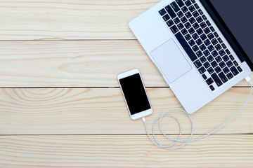Smartphone connected to laptop on wooden table with copy space.