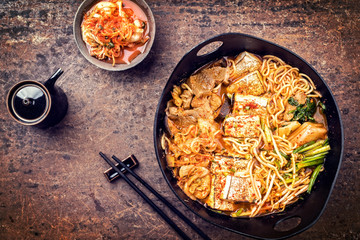 Traditional Korean kimchi jjigae with grilled pork belly and ramen as top view in a modern design Japanese cast-iron roasting dish - vintage