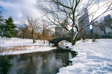 Winter sun streaming over the snow-covered landscape of the stone arch Gapstow Bridge in Central Park against the skyline of Midtown Manhattan after a blizzard in New York City