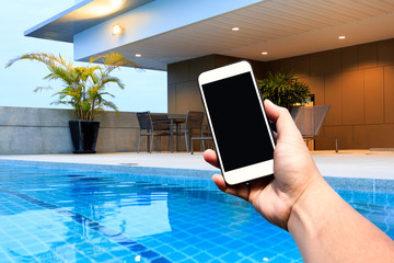 Hand hold Modern smartphone with blank screen at outdoor swimming pool and terrace upper deck. Copy space.